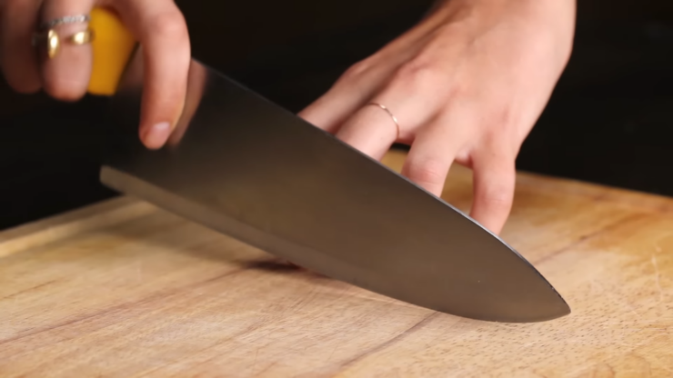 Hand Holding a Kitchen Knife Close to Fingers on A Wooden Cutting Board