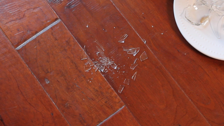 Broken Glass Pieces Scattered on A Wooden Floor Near a Plate