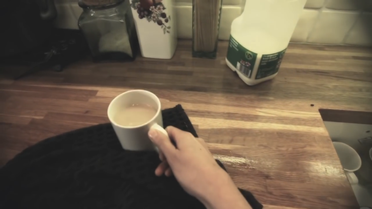 Hand Holding a Cup of Hot Liquid on A Wooden Countertop